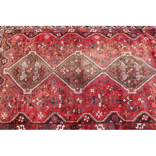 1215 - Persian handwoven wool carpet of red ground, with central diamond design, showing age & wear, cut do... 