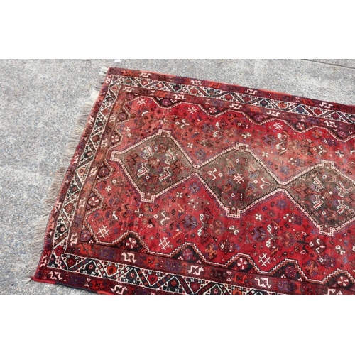 1086 - Persian handwoven wool carpet of red ground, with central diamond design, showing age & wear, cut do... 