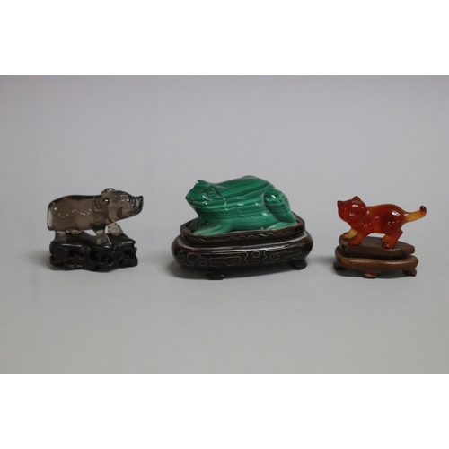 114 - Chinese Malachite carving of a frog, a crystal carved pig and a carnelian cat all on wooden stands, ... 