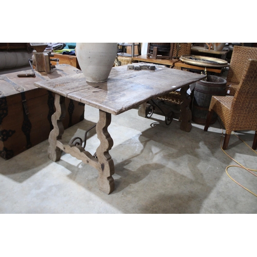 585 - Antique Spanish walnut trestle table, with trestle ends joined by a scrolling iron stretcher, approx... 