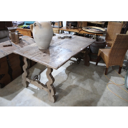 585 - Antique Spanish walnut trestle table, with trestle ends joined by a scrolling iron stretcher, approx... 