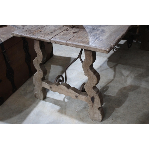 585 - Antique Spanish walnut trestle table, with trestle ends joined by a scrolling iron stretcher, approx... 