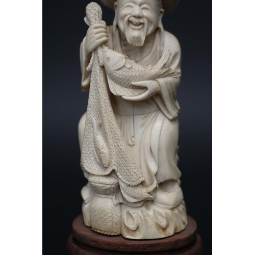 12 - Fine carved ivory figure of an elderly fisherman, holding fish & net, on wooden stand with silver in... 