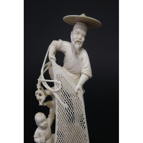 23 - Finely carved ivory figure of an old fisherman hauling in his net, with young boy, standing on woode... 