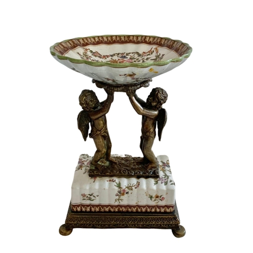 434 - Wong Lee 1895 ornate brass and porcelain pedestal bowl/comport. With cherub figures. 23x17x33.5cm