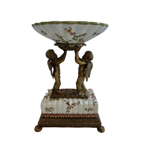 434 - Wong Lee 1895 ornate brass and porcelain pedestal bowl/comport. With cherub figures. 23x17x33.5cm