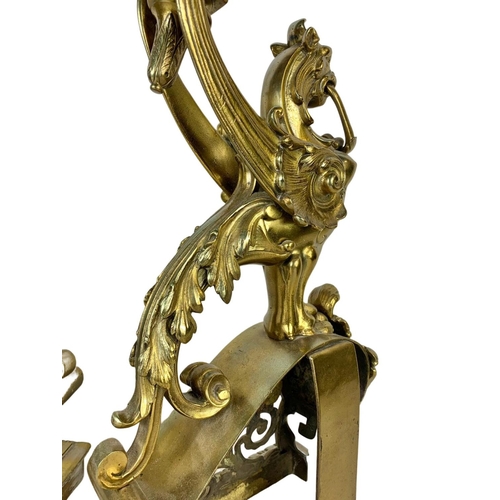 324u - A pair of large early 20th century ornate brass andirons in the form of griffins. 53cm.