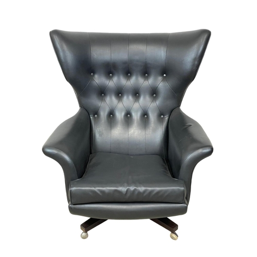 902 - A G-Plan “Blofeld” wingback swivel armchair in black vinyl and on a rosewood base. Model 6250R. 1962... 