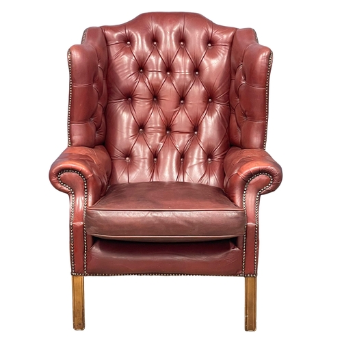 868 - A large Georgian style deep button ox-blood leather wingback armchair.