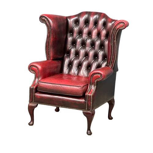 1006 - An ox-blood deep button leather wingback armchair. (5)