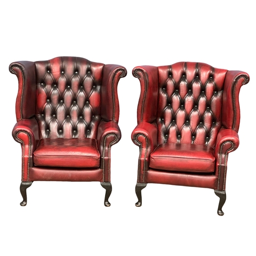 839 - A pair of ox-blood deep button leather wingback armchairs. (7)