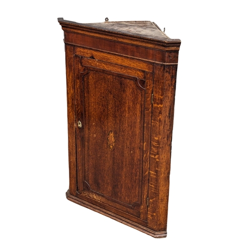 1063 - A George III inlaid oak wall hanging corner cabinet with fitted shelves. Circa 1790-1800. 69.5x38.5x... 