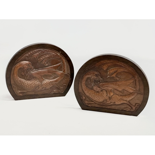 32 - A pair of Late 19th/ Early 20th Century bookends with embossed dragon leather panels in oak frames a... 