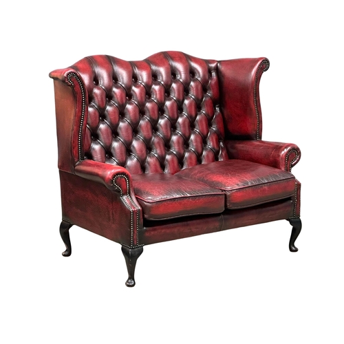 151 - An ox-blood deep button leather 2 seater wingback sofa. 136cm. (5)