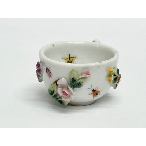 141 - Sitzendorf. A Late 19th/Early 20th Century German flower encrusted miniature cup and saucer, with pa... 