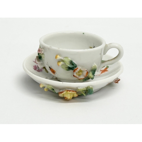 141 - Sitzendorf. A Late 19th/Early 20th Century German flower encrusted miniature cup and saucer, with pa... 