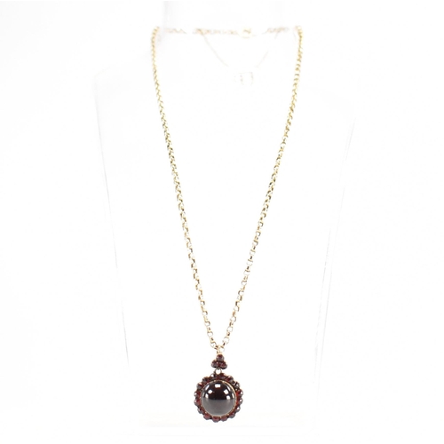 215 - An antique garnet locket on a gold chain. The Victorian locket being set with central garnet cabocho... 