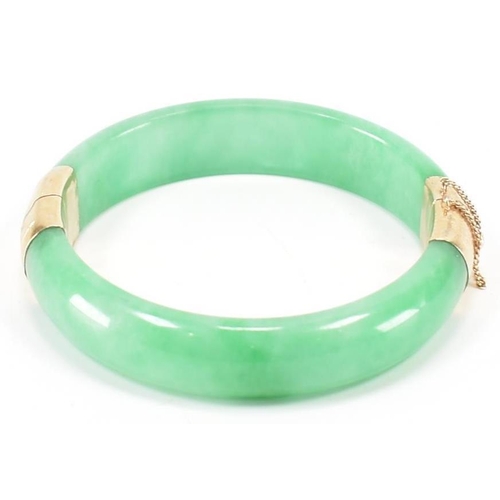 226 - A vintage green jade and gold plated bangle bracelet. The bracelet having gold plated fittings with ... 