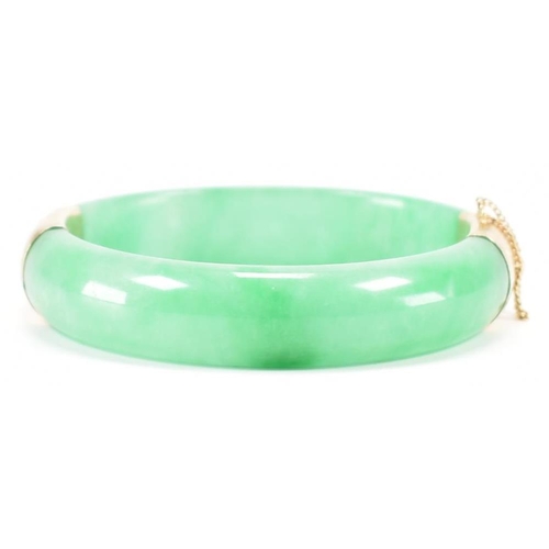 226 - A vintage green jade and gold plated bangle bracelet. The bracelet having gold plated fittings with ... 