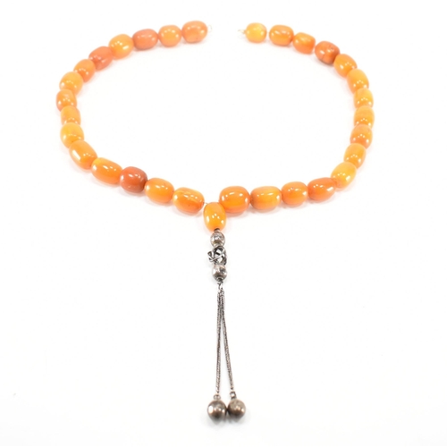 249 - An antique amber and silver necklace. The necklace being strung with twenty five barrel shaped beads... 