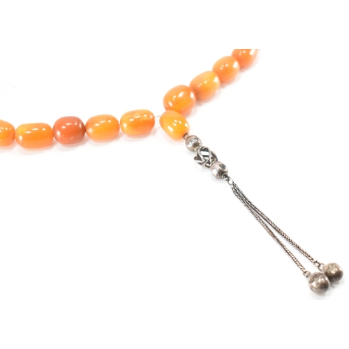 249 - An antique amber and silver necklace. The necklace being strung with twenty five barrel shaped beads... 