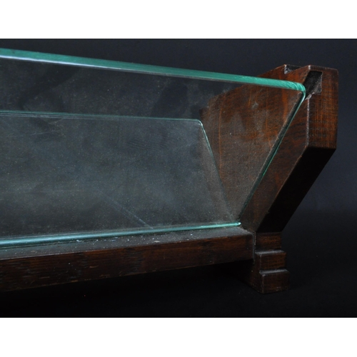 1474 - A 1930's Art Deco solid oak and glass book trough. Of angular form with shaped ends having sliding g... 