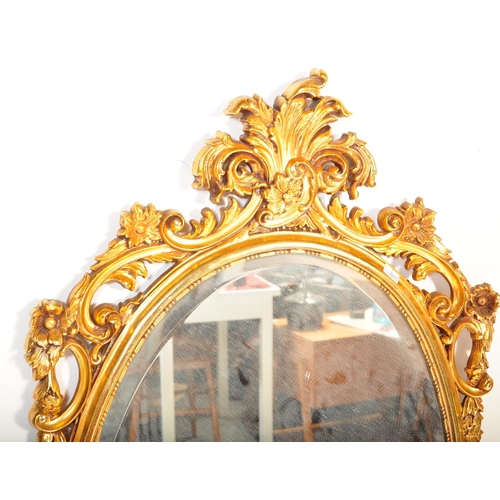 1504 - A Veronese product made in England. A gilt hanging wall mirror. Of oval form with scroll foliate dec... 