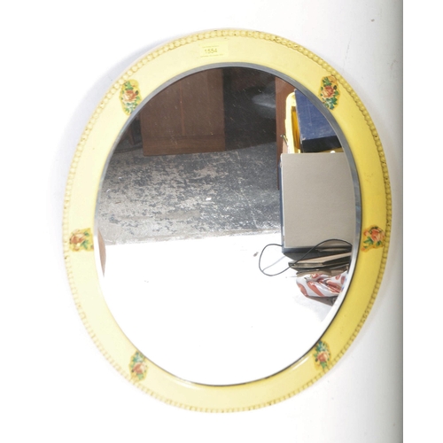 1523 - A yellow painted oval folk bevelled mirror. The mirror with a beaded decorated border with floral / ... 