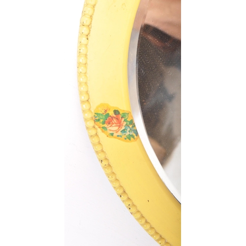 1523 - A yellow painted oval folk bevelled mirror. The mirror with a beaded decorated border with floral / ... 