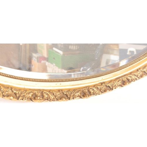 1555 - A pair of gilt framed bevelled edge mirrors. One of oval form with a beaded border and geometric pat... 