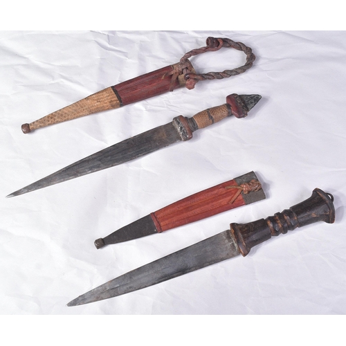 298 - Two North African tribal knives / daggers. Both with tapering blades housed in tooled leather scabba... 