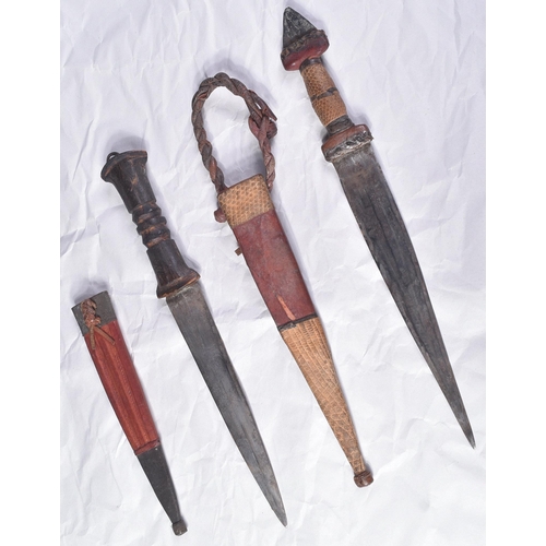 298 - Two North African tribal knives / daggers. Both with tapering blades housed in tooled leather scabba... 