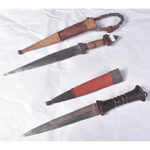 298 - Two North African tribal knives / daggers. Both with tapering blades housed in tooled leather scabba... 