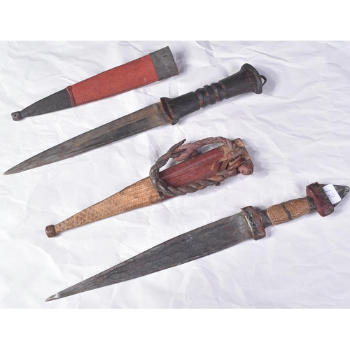 298 - Two North African tribal knives / daggers. Both with tapering blades housed in tooled leather scabba... 