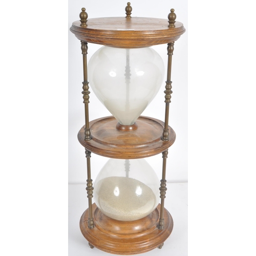 186 - A large 20th Century floor standing hourglass of typical form having a stained pine frame and brass ... 