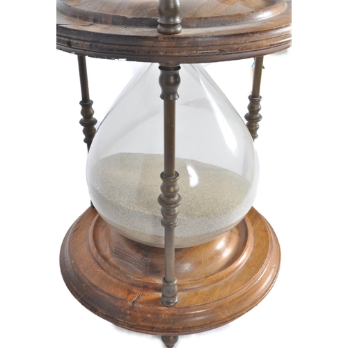 186 - A large 20th Century floor standing hourglass of typical form having a stained pine frame and brass ... 