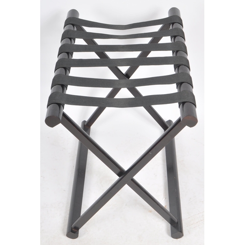 546 - A matching pair of Contemporary ebonised luggage rack stands with webbed tops and folding X-frame st... 