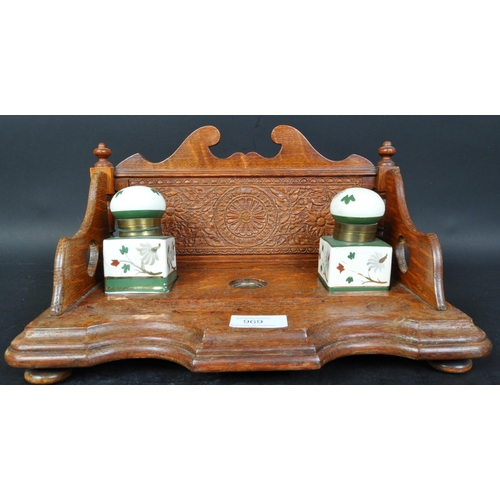 384 - A vintage 20th Century oak ink stand. Having a decorated carved back, with two ceramic hand painted ... 