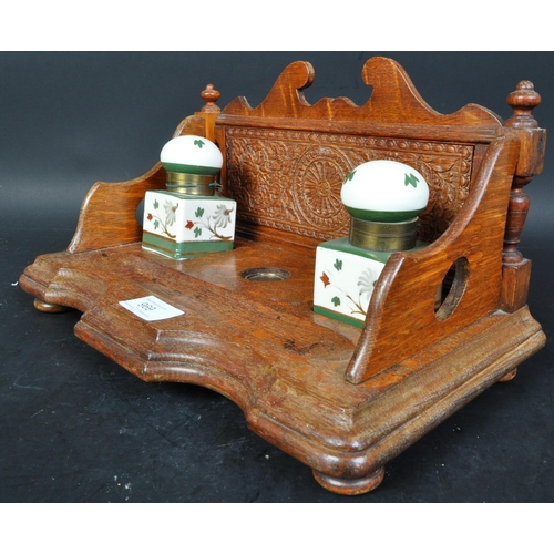 384 - A vintage 20th Century oak ink stand. Having a decorated carved back, with two ceramic hand painted ... 