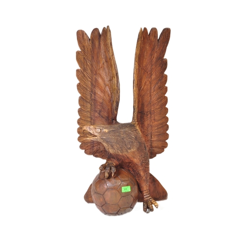 636 - A vintage 20th century carved wooden sculpture of an eagle with upstretched wings resting on footbal... 