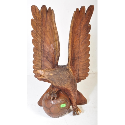 636 - A vintage 20th century carved wooden sculpture of an eagle with upstretched wings resting on footbal... 