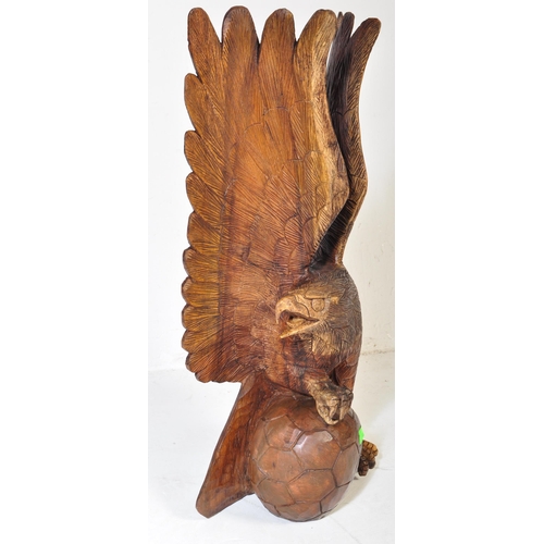 636 - A vintage 20th century carved wooden sculpture of an eagle with upstretched wings resting on footbal... 