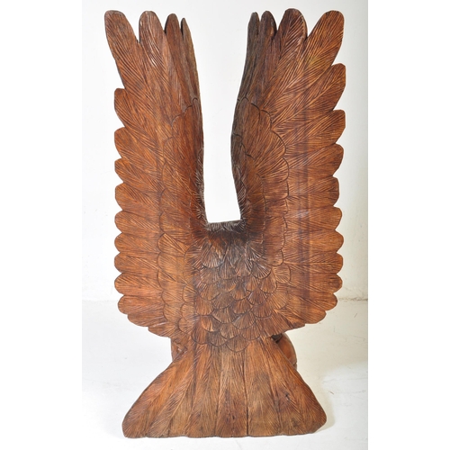 636 - A vintage 20th century carved wooden sculpture of an eagle with upstretched wings resting on footbal... 