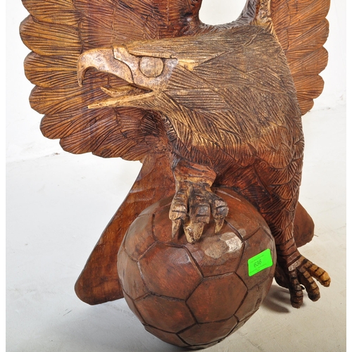 636 - A vintage 20th century carved wooden sculpture of an eagle with upstretched wings resting on footbal... 