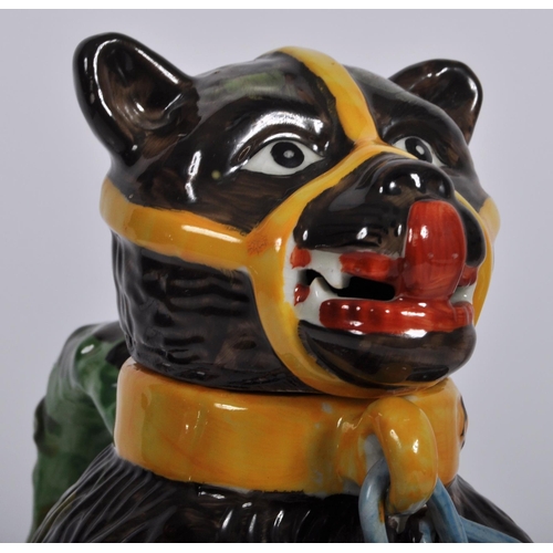 227 - A bear baiting advertising jar and cover, modelled as a large bear clutching a snarling dog between ... 