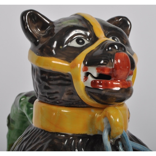 227 - A bear baiting advertising jar and cover, modelled as a large bear clutching a snarling dog between ... 