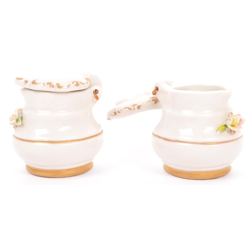 133 - A vintage 20th Century Capodimonte marked porcelain inkwell and two jugs, with china flower relief t... 