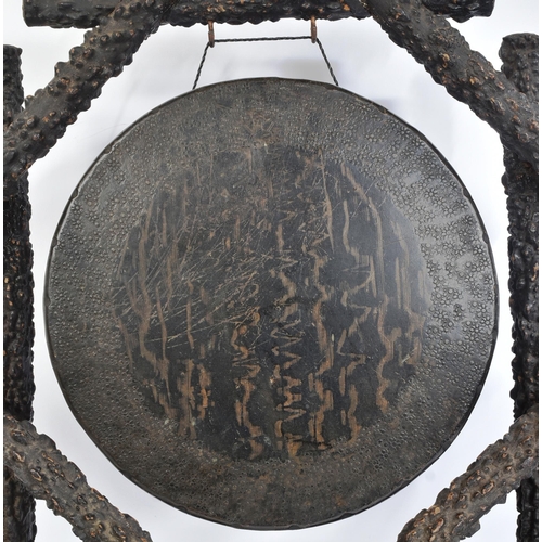 237 - A 19th century Burmese brass and hardwood dinner gong. Shaped hardwood stand, each support with a br... 