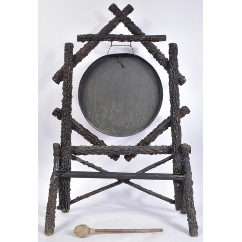 237 - A 19th century Burmese brass and hardwood dinner gong. Shaped hardwood stand, each support with a br... 