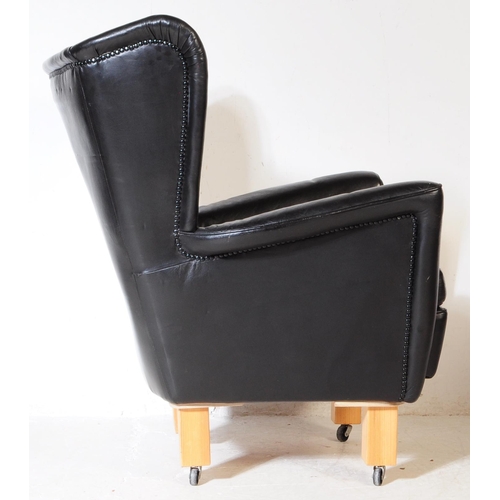 572 - G Plan - A mid 20th century G-Plan batwing black faux leatherette vinyl armchair being raised on lat... 